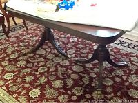 Full view of the antique dining table with double pedestal legs placed on a patterned red carpet, showing its overall size and shape.