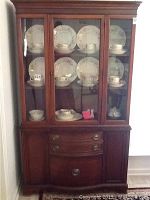 Front view of antique wooden china cabinet with glass doors showing displayed plates and teacups inside.