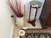 Butter churn, wooden stick, and marble plant stand placed on floor by wall with vase and carpet
