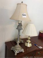 One brass lamp 12 inches tall with cream pleated lampshade and two matching taller pineapple motif lamps with distressed finish and bell-shaped fabric shades.