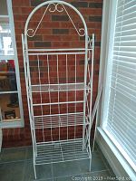 Front view of white metal shelf with decorative scrollwork and multiple Plexiglass-covered shelves.