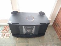 Top view photo showing RCA stereo system inside a black entertainment stand with curved glass doors, also showing two black RCA speakers placed on top of the stand.