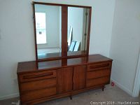 Full view of mid-century wooden dresser with attached large rectangular mirror in a wooden frame