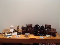 Full view of table showing assorted jewelry including rings, watches, stick pins with protective clutches, wooden and metal storage boxes, and various small collectibles.