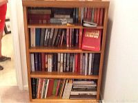 Full view of the wooden bookshelf containing four shelves filled with assorted books and magazines.