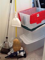 Overview of smaller vacuums, broom, dustpan, and stacked plastic bins