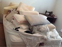 Bed with mattress and box spring covered with assorted pillows, quilts and blankets piled on top.