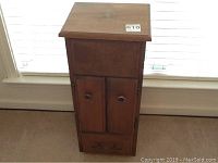 Full front view of small wooden cabinet showing two doors and a bottom drawer with metal knobs.