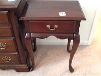 Photo showing the full wooden end table with single drawer, curved legs, and brass handle.