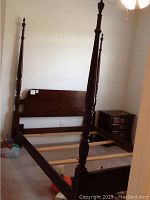 Full view of assembled wood poster bed frame in a room showing headboard, footboard, and side rails.