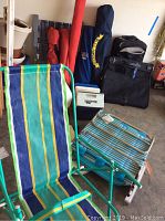Four striped fabric folding camp chairs with green metal frames in storage bags, three coolers stacked against wall, tennis rackets and dumbbells in background