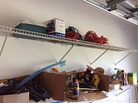 Wide view of two wire shelves with assorted garage items including orange extension cords, rope, spray cans, and hand tools in boxes.