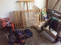 Overview of lot showing hose reel cart with green garden hose, Black & Decker cordless sweeper, wooden baby gates and rake, ceramic flower pot, and weed killer container on garage floor.