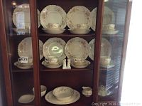 Full display of Homer Laughlin China set in cabinet showing plates, cups, bowls, and salt and pepper shakers with floral trim and gold highlights.
