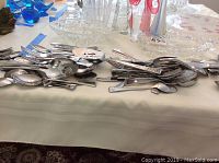 Photo showing a pile of assorted stainless steel cutlery with forks, spoons, and knives on a table.