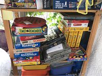 Stack of assorted vintage board games including Times to Remember, Scrabble, Sorry!, Advance to Boardwalk, Eye Guess, The Simpsons Loser Takes All, and puzzles in plastic containers
