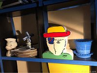 Shelf view showing all items: pig pitcher, windmill figurine, plates, Peter Max cookie jar, glass planter