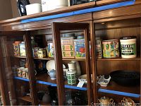 Photo of wooden display cabinet with multiple vintage label ceramic jars with lids and kitchen items inside