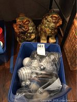 Blue bin holding multiple decorative glass balls in monochrome colors and patterns, two ceramic Foo Dog statues behind