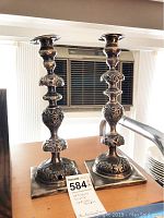 Pair of candlesticks displayed on tabletop under overhead light.