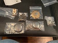 All items arranged on black surface in ziplock bags showing set contents including pocket watches, locket, chains, sweater guards and small accessories.