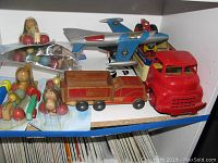 Shelf with a metal blue and silver toy airplane, a red wooden truck marked Holcate Toys, and wooden pull toys with colorful balls shaped as animals