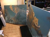 Two large canvases leaning against wall, showing both cloudscape paintings
