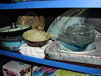 Shelf displaying multiple stacked ashtrays including green ceramic with lighter, blue ceramic, clear glass, gold-toned, rusted metal ashtrays