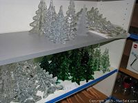 Shelf with various clear, frosted, and iridescent glass Christmas trees of multiple sizes arranged in rows.