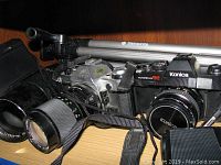 Photo of Konica Autoreflex TC camera with lens, Canon film camera with lens, and Samsonite tripod on shelf.