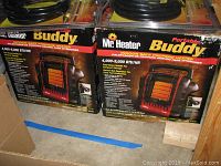 Two boxed Mr. Heater Portable Buddy heaters side by side with hoses on top