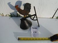 The whole cast iron rooster bell showing the mounting bracket and approximate size using a tape measure.