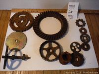 Top-down view of all 12 gears showing varying sizes and shapes, largest measuring approx 8.5 inches, arranged on a white board with ruler for scale.