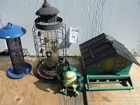 View of all four bird feeders and ceramic frog on wooden surface against white wall