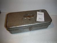 Closed old metal fishing tackle box showing latch closure and handle with fishing brand name plate on lid.
