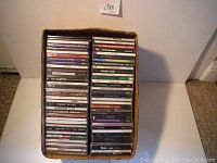 Box containing 75 music CDs stacked vertically showing various spine titles in original jewel cases.