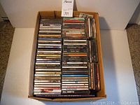 Box of CDs stacked vertically showing spines with artist names and album titles including All Saints, The Cranberries.