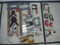 Photo showing all 16 clamps arranged on concrete board, including bar clamps, spring clamps, and C-clamps.