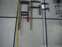 Overview photo showing three F clamps laid out on the ground with tape measure for size reference.