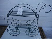 Front and side view showing size, tier shelves, decorative wheels, scrolled wire handle, and overall structure of the metal plant stand.