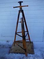 Full view of the tall orange metal adjustable work stand with stable base and threaded screw central mechanism for height adjustment.