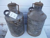 Two large vintage Imperial Oil metal cans with lids and side handles, showing rust and dent wear