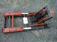 Top view of ATV lift jack showing hydraulic pump, handle, and lifting platforms with some rust and dust.