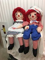 Full frontal view showing the Raggedy Ann and Andy dolls seated, dressed in their classic attire with visible facial features and yarn hair.