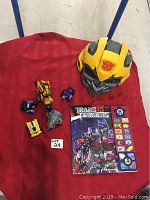 Lot displayed on red cloth showing yellow Transformer mask, six small Transformer figures, and Transformers sound book.