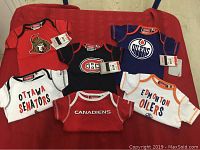 Six NHL hockey baby onesies laid out on red surface, showing Ottawa Senators, Montreal Canadiens, and Edmonton Oilers designs.