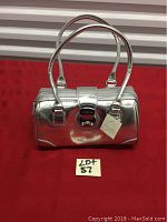 Front view of the silver Liz Claiborne purse showing full shape and handles against red background.