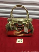 Gold Liz Claiborne purse front view with double handles, lock clasp, and visible tags shown on red background.