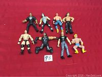 Eight wrestling action figures arranged on a red surface, showing front view to highlight details and costumes.