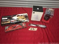 Photo of the lot on red surface including Clever Cutter 2 in box, white kettle box, Master Cut knife set with knives, cream and sugar set.